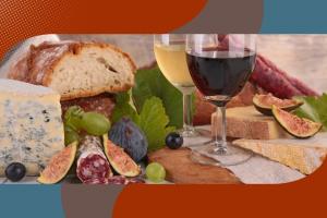 Composizione enogastronomica con calici di vino rosso e bianco, formaggi assortiti, salame, fichi freschi, uva e pane su un tagliere in legno