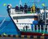Prua di una nave da carico ormeggiata in banchina con membri dell'equipaggio a bordo.