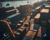 Veduta dall'alto di un porto commerciale con container colorati, operatori con caschi protettivi e un camion, illuminati dalla luce calda del sole.